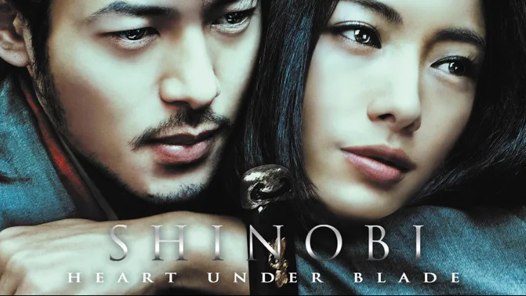Foto close-up poster film Shinobi: Heart Under Blade menampilkan wajah dua karakter utama; pria di sisi kiri (Gennosuke) dengan kumis dan janggut tipis menatap ke bawah, dan wanita di sisi kanan (Oboro) dengan rambut hitam panjang menatap ke arah depan dengan ekspresi melankolis; terdapat teks judul "SHINOBI HEART UNDER BLADE" di bagian bawah gambar.